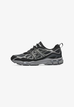 Baskets de sport noires et grises avec tige en mesh et synthétique, semelle épaisse rembourrée, fermeture à lacets et languette à l’arrière sur fond blanc.