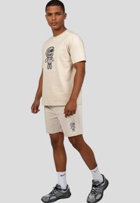 Beige cotton t-shirt with graphic printed design of a character on the front, paired with matching beige shorts featuring a smaller graphic.