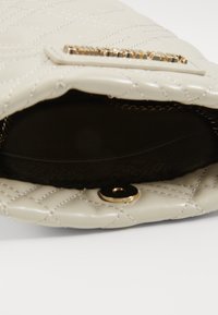 Borsa in pelle crema trapuntata con minuteria dorata. L'interno è scuro con un motivo di rivestimento e presenta una chiusura a scatto. Design compatto.