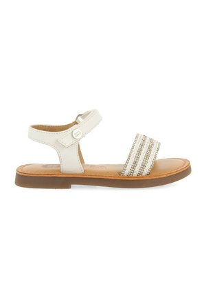 Sandal de cuero blanco con una suela plana color marrón, que presenta una tira ancha adornada con acentos tejidos en plata y blanco, y un cierre de hebilla lateral.