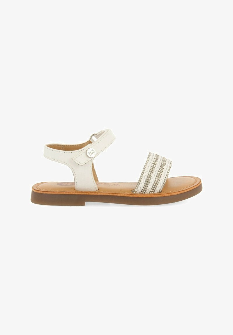 Sandal de cuero blanco con una suela plana color marrón, que presenta una tira ancha adornada con acentos tejidos en plata y blanco, y un cierre de hebilla lateral.