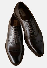 Zapatos oxford de cuero marrón con puntera cap y diseño de alerones, detalles texturizados a lo largo de las costuras y cierre de cordones tradicional.