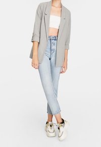 Blazer rayé gris porté sur un crop top blanc, associé à un jean taille haute bleu clair et des baskets blanches avec des accents jaunes et noirs.