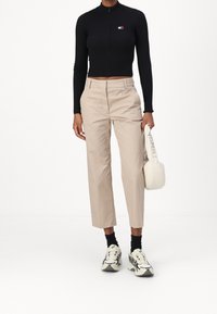 Top negro de canalé con cremallera, pantalones beige ajustados, bolso blanco de hombro y zapatillas gruesas con acentos en negro y crema.