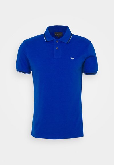 Πολό μπλουζάκι σε φωτεινό μπλε βαμβάκι με κλασικό γιακά, πλάκα με δύο κουμπιά και αντίθετες μαύρες και λευκές ρίγες στις μανσέτες.