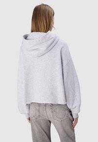 Haut à capuche cropped gris clair avec une grande capuche, des épaules tombantes et un ourlet brut. Assorti avec un jean gris délavé présentant des coutures distinctives.