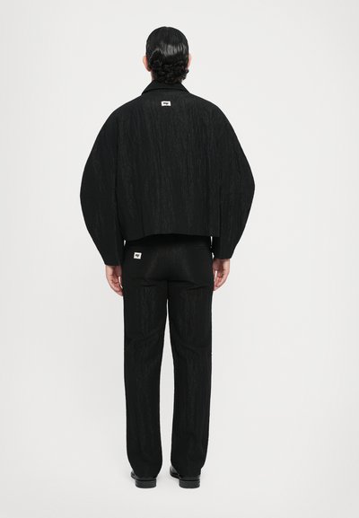 Schwarze leichte strukturierte Jacke mit gesenkten Schultern, kombiniert mit passenden, schmal zulaufenden Hosen. Beide verfügen über dezente Markenetiketten.