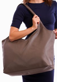 Brown leather tote bag with a curved, spacious design. Features a single shoulder strap and subtle brand logo embossed on the front.