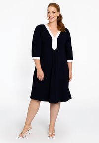 Dunkelblaues Kleid mit V-Ausschnitt und weißen Details. Mit puffärmel und ausgestelltem Schnitt. Glattes Material mit matter Oberfläche.