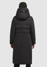 Crni kaput s punjenjem i kapuljačom, s kviltanom izradom, dugim rukavima i logotipom na stražnjem dijelu. Glatka tekstura, do koljena.