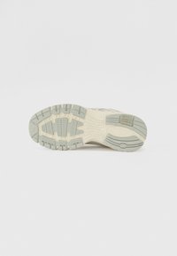 Semelle de chaussure de course avec une surface en caoutchouc texturé de couleur beige clair, dotée de rainures et de crampons pour une meilleure traction. Accents en vert subtil.