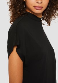 Haut noir à manches courtes avec un col haut, fabriqué en tissu lisse. Présente des coutures d'épaule arrondies et une coupe décontractée.