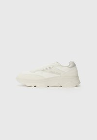 Fehér sneaker, sima és suede textúrák kombinációjával, vastag talppal, geometrikus mintákkal és perforált részletekkel az oldalán.