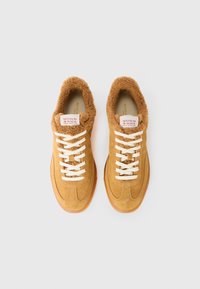 Brune suedesneakers med en fluffy brun krage, hvite snørebånd og en gummisåle. Har et merke på tungen som sier "SCOTCH & SODA AMSTERDAM."