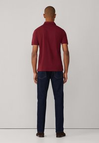 Poloko s krátkym rukávom v burgundskej farbe s rovnými okrajmi, v kombinácii s tmavomodrými džínami a hnedými topánkami, z pohľadu zozadu.