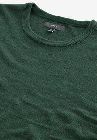 Suéter verde de punto hecho de material suave, con cuello redondo y una textura sutil. La etiqueta dice "NEXT", tamaño M.