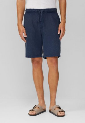 Shorts bleu marine avec une taille élastique et un cordon de serrage, présentant un design décontracté et une texture légère. Portés avec des sandales marron.