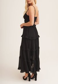 Black maxi dress with layered ruffles, thin straps, and a lightweight material. Worn with black high-heeled shoes.