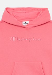 Felpa in cotone rosa con logo "Champion" ricamato, tasca frontale e cappuccio con coulisse. Texture morbida e design casual.