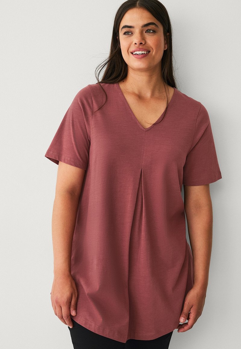 Korte mouwen, V-hals top in rozenkleurige stof met plooidetail aan de voorkant, een gladde textuur en een ontspannen pasvorm, gecombineerd met donkere onderkleding.