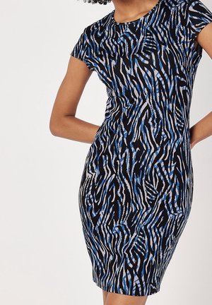 Frau trägt ein kurzes, tailliertes Kleid mit einem abstrakten, schwarzen, blauen und weißen wellenförmigen Streifenmuster.