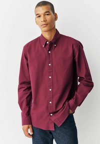 Bordeaux knoopshirt met lange mouwen, witte knopen en een klein logo op de linkerborst. Gemaakt van een gladde stof, slim fit.