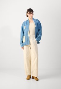 Svetlomodrá oversized denim bunda s krémovými akcentmi, krémová plisovaná blúzka a béžové nohavice so širokými nohavicami. Hnedé členkové topánky na podpätku.