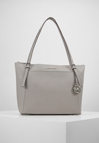 Grijze leren tote bag met twee schouderbanden, voorzien van een ritssluiting, gegraveerd logo en metalen charme accent. Gladde textuur, rechthoekige vorm.