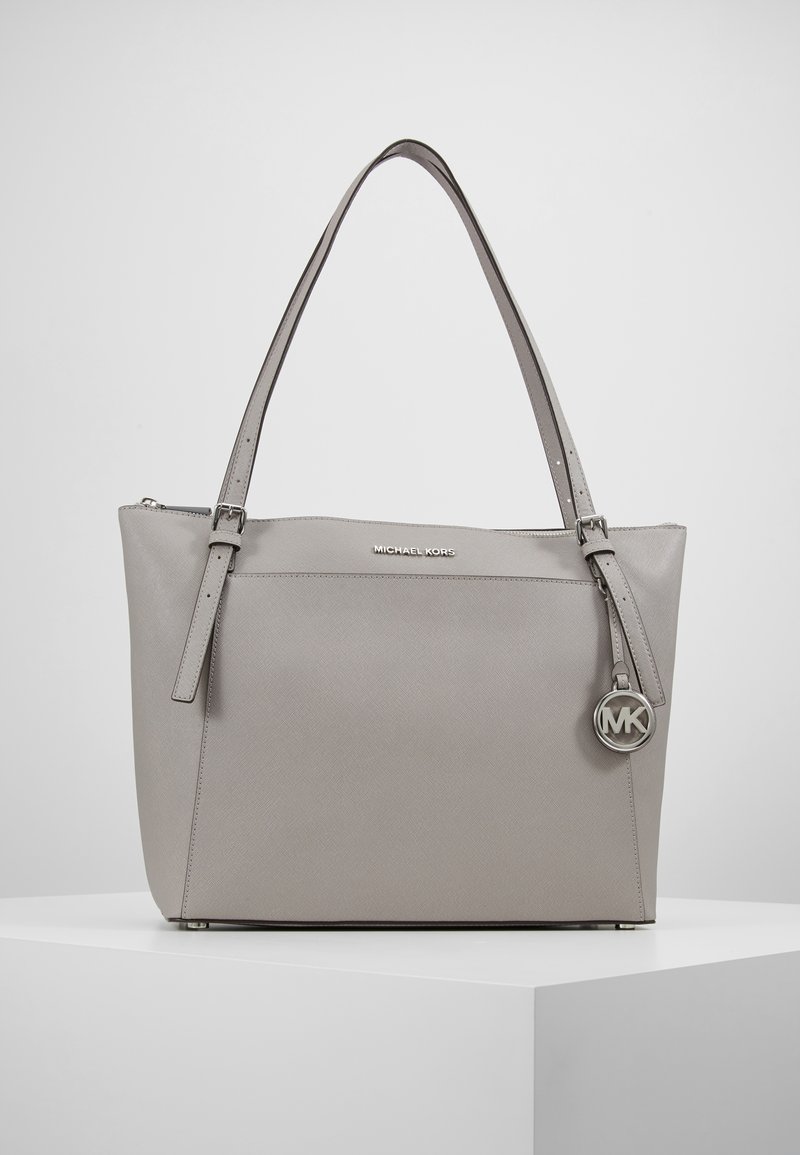 Grijze leren tote bag met twee schouderbanden, voorzien van een ritssluiting, gegraveerd logo en metalen charme accent. Gladde textuur, rechthoekige vorm.