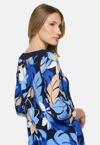 Top s květinovým vzorem v odstínech modré, námořnické modři a krémové, s tříčtvrtečními rukávy a kulatým výstřihem. Měkká látka s hladkou texturou.