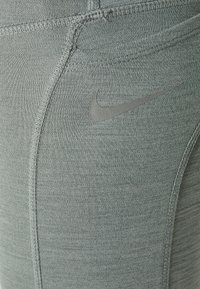 Leggings deportivos grises con una tela texturizada. Incluye costuras en contraste y un pequeño logo negro de Nike en el costado.