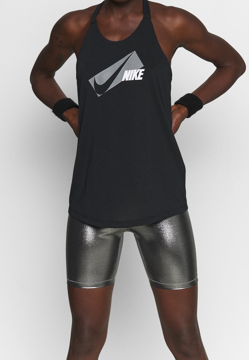 Musta Nike-toppi, jossa on hopeinen logo, yhdistetty metallinhohtoisiin hopeisiin pyöräilyshortseihin. Omistaa halterneck-mallin ja sileän tekstuurin.
