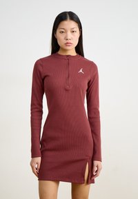Abito lungo bordeaux a maniche lunghe con colletto zip, texture a costine, spacchi laterali e un piccolo logo bianco sul petto.