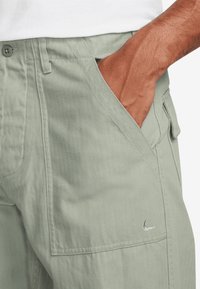 Light green cargo shorts made of durable fabric with a textured surface, featuring side pockets and a small logo detail on the edge.
