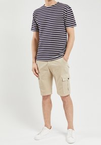 Navy and white striped cotton t-shirt, paired with beige cargo shorts featuring side pockets. Model wears white sneakers.