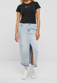 Mustaa lyhythihaista t-paitaa, jossa on valkoinen graafinen kuvio, yhdistettynä vaaleansinusiniseen farkku-maksihameeseen, jossa on edessä halkio. Valkoiset tennarit viimeistelevät asun.