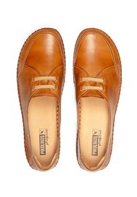 Zapatos de cuero marrón con forma redondeada, detalles cosidos y tiras elásticas. Textura suave con un forro interior cómodo.