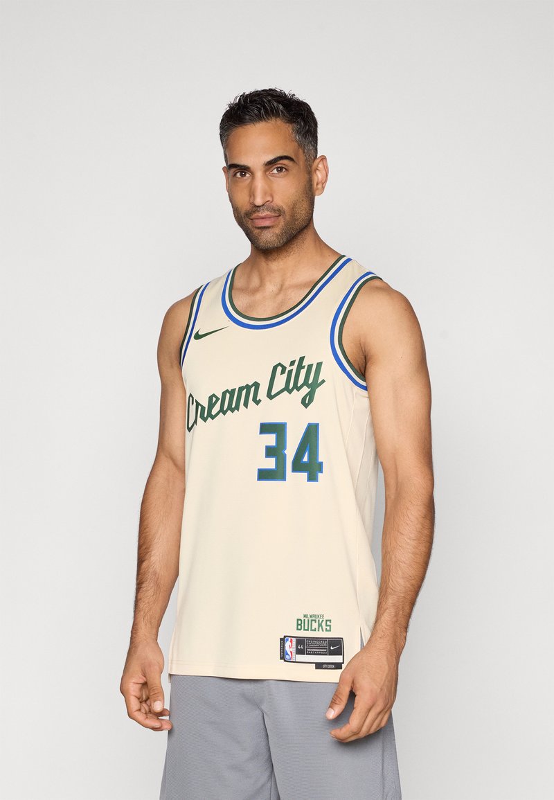 Béžový basketbalový dres s nápisom "Cream City" v zelenom písme a číslom "34" v tučnej zelenej. Modré a zelené lemovanie. Logo Nike a značka NBA sú zahrnuté.