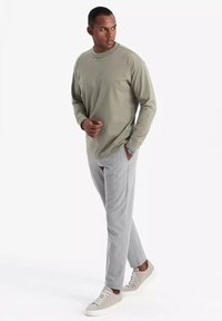 Camisa de manga larga verde oliva claro, pantalones grises a rayas y zapatillas grises. La tela parece suave, con un ajuste holgado y un mínimo de detalles.