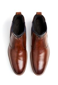 Bottines en cuir marron avec une finition lisse, inserts élastiques sur les côtés et languettes de traction. L'intérieur est doté d'un revêtement doux pour le confort.