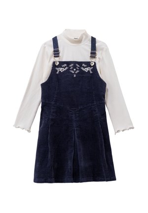 Marinefarbene Corduroy-Latzkleid mit verstellbaren Trägern und Blumenstickerei, kombiniert mit einem gerippten weißen Rollkragenpulli mit gewellten Säumen.