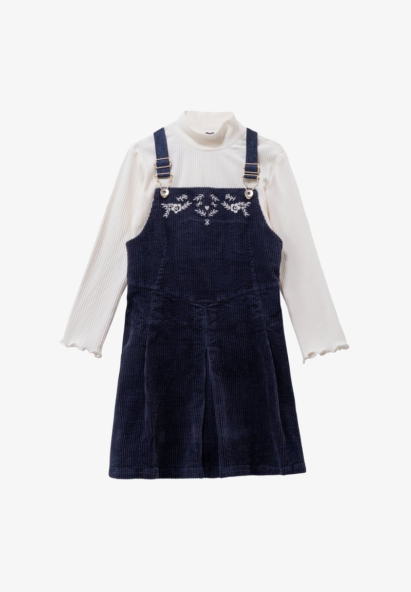 Granatowa sukienka ogrodniczka z kordurowego materiału z regulowanymi ramiączkami i haftem w kwiaty, zestawiona z ryżowym białym swetrem polo z falbaniastymi mankietami.