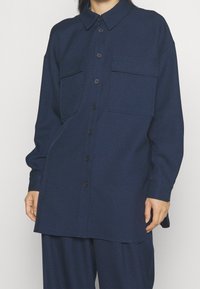 Marinblå knapp-up skjorta i texturerad fabric, med två bröstfickor, krage och en avslappnad passform med böjd nederkant.