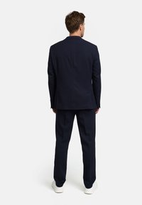 Navy blauw pak met een blazer met twee knopen en rechte broek, op maat gemaakt, gecombineerd met witte sneakers, gezien van achteren.