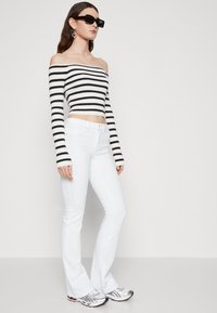 Svart og hvit stripete off-shoulder crop topp med lange ermer, kombinert med hvite slengjeans og sølvfargede treningssko.