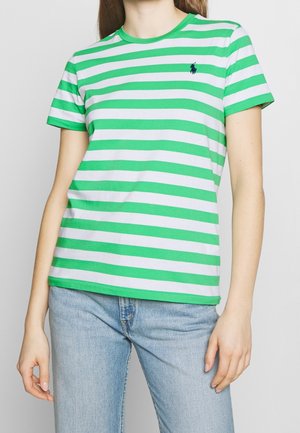 Górna część ciała ubrana w zielono-białą koszulkę w paski z krótkim rękawem i małym ciemnoniebieskim logo na lewej piersi oraz jasnoniebieskie dżinsy.