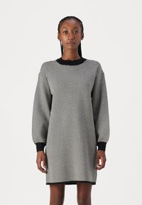 Vestido com padrão zigzag em preto e branco, com gola e punhos ribados em preto, apresentando um corte solto e comprimento até a metade da coxa. Textura suave.