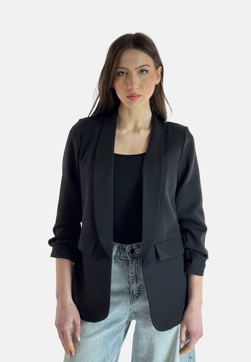 Blazer nero su misura con colletto a scialle, due tasche frontali e maniche leggermente arrotolate, abbinato a jeans azzurri a vita alta.