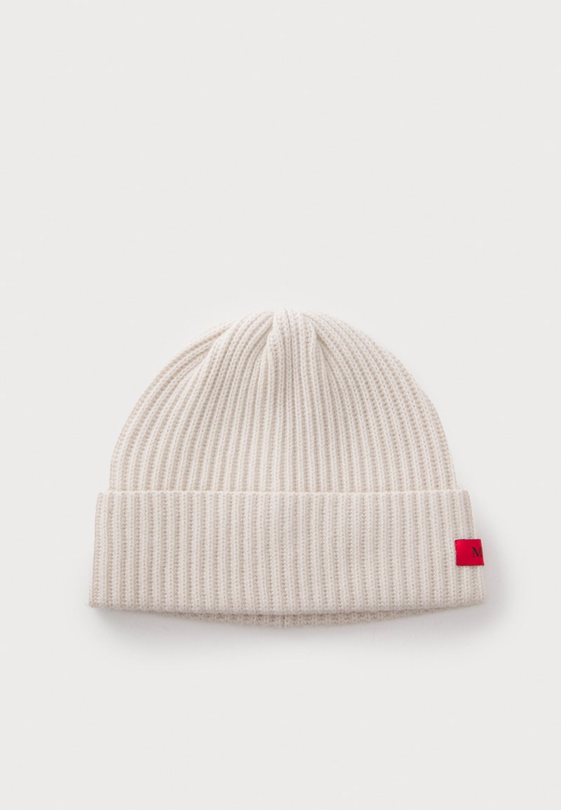 Cream-colored ribbed knit beanie with folded cuff and small red tag on the side against a white background.
