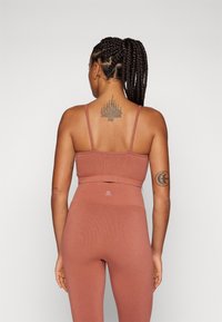 Ribbede sports-bh og leggings-sett i dempet terrakotta. Har tynne stropper, høy midje og teksturert stoff med logodetaljer.